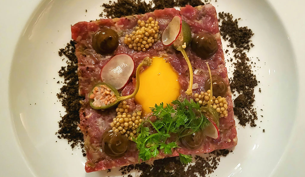 Rindfleisch-Tatar mit schwarzem Knoblauch, gegartem Eigelb und Senfkörnern. Foto: Christian Euler
